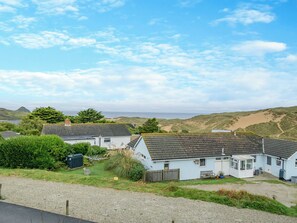 Una casa costera con camino de grava, patio cercado y vista al mar y las colinas.