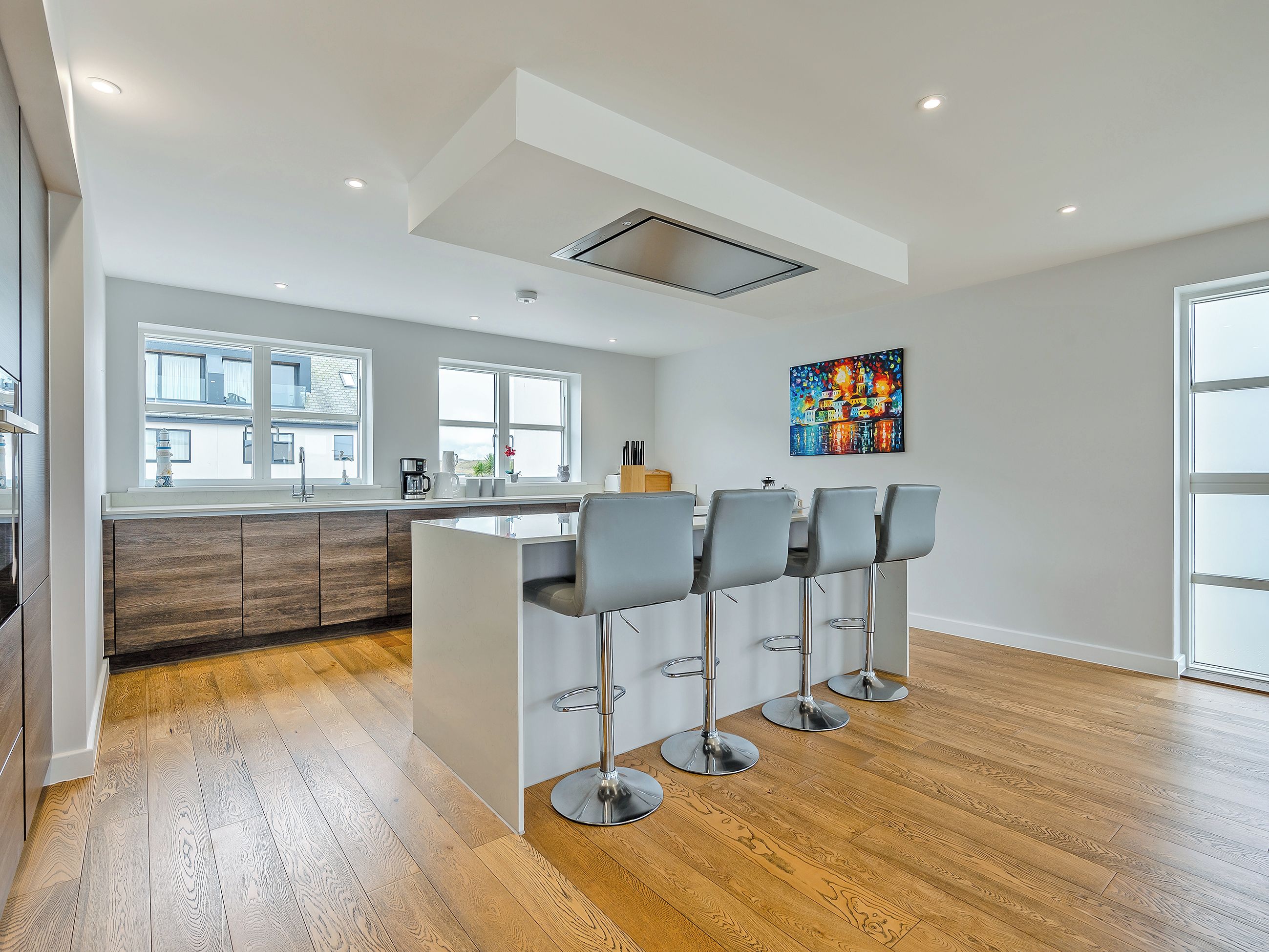 A modern kitchen with a central island, bar stools, and a large window.