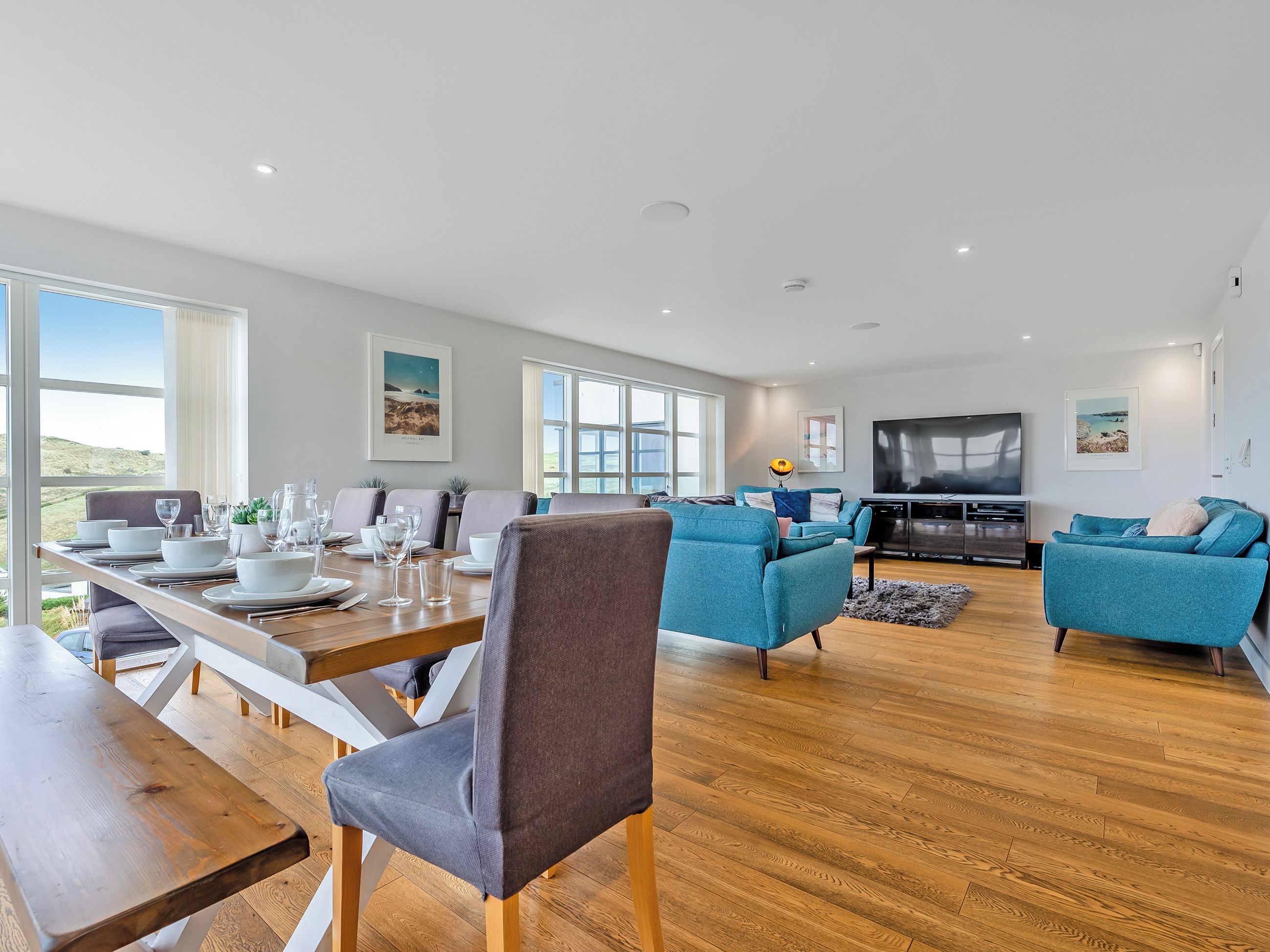 A modern living room with a dining area, large windows, and a flat-screen TV.