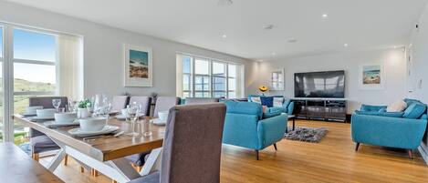 A modern living room with a dining area, large windows, and a flat-screen TV.