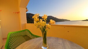 A balcony with a wooden table and a vase of yellow flowers, overlooking a body of water and a hilly landscape. - Seafront Apartments Anthony (Lastovo)