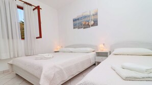 A hotel room with two beds, white bedding, a painting of a beach scene, and a window with curtains. - Seafront Apartments Anthony (Lastovo)