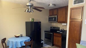 A compact kitchen with a refrigerator, microwave, stove, and sink. There is a dining table with chairs and a ceiling fan. - Cozy Nob Hill Condo close to UNM (Albuquerque)