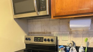 A kitchen with a stainless steel stove, oven, and microwave. There is a sink with a faucet and a dish soap dispenser. A red towel hangs on the oven door, and a white towel is on the countertop. - Cozy Nob Hill Condo close to UNM (Albuquerque)