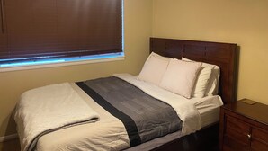 A neatly made bed with a headboard, a bedside table, and a window with blinds. - Cozy Nob Hill Condo close to UNM (Albuquerque)