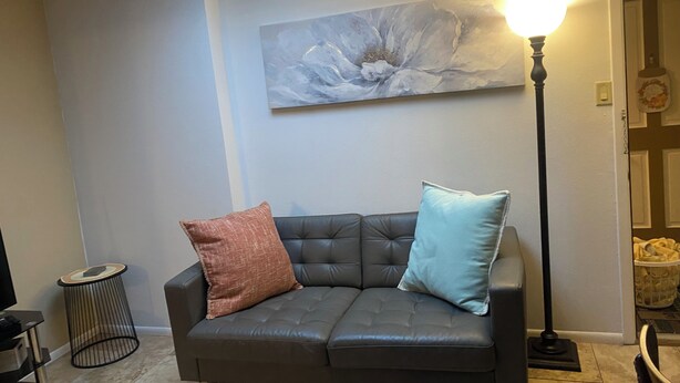 A living room with a dark leather sofa, two cushions, a round side table, a floor lamp, and a large abstract painting on the wall. - Cozy Nob Hill Condo close to UNM (Albuquerque)