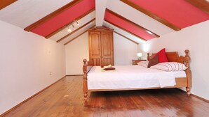 Un dormitorio con una cama de madera, una mesita de noche, un armario y un techo inclinado con vigas a la vista.