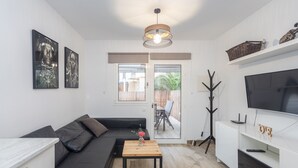 Una sala de estar moderna con un sofá de cuero negro, una mesa de centro de madera, un televisor sobre un soporte blanco y un amplio ventanal con vistas a un patio.