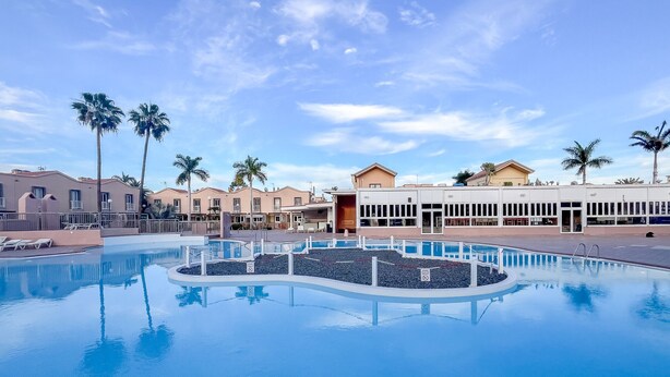 Una piscina con una isla circular, palmeras y edificios al fondo.