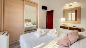 Una habitación de hotel con cama, armario, espejo, televisor y mesita de noche.