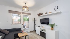 Una sala moderna con un sofá negro, una mesa de centro de madera, un televisor sobre un soporte blanco y una planta en maceta.