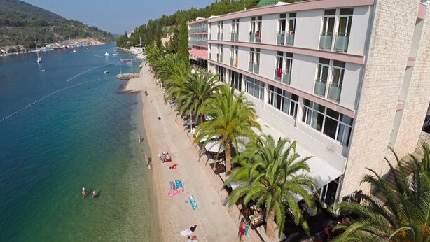 A coastal hotel with a beachside location, featuring a row of palm trees and a clear view of the sea. - Marconi Charming Apartments (Vela Luka)