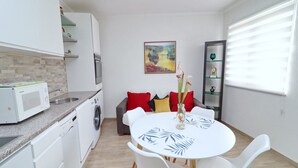 A compact kitchen with a microwave, washing machine, and a dining area with a round table and chairs. - Marconi Charming Apartments (Vela Luka)