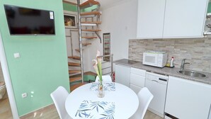 A compact kitchen with white cabinets, a microwave, and a sink. There's a dining table with chairs and a vase with flowers. - Marconi Charming Apartments (Vela Luka)