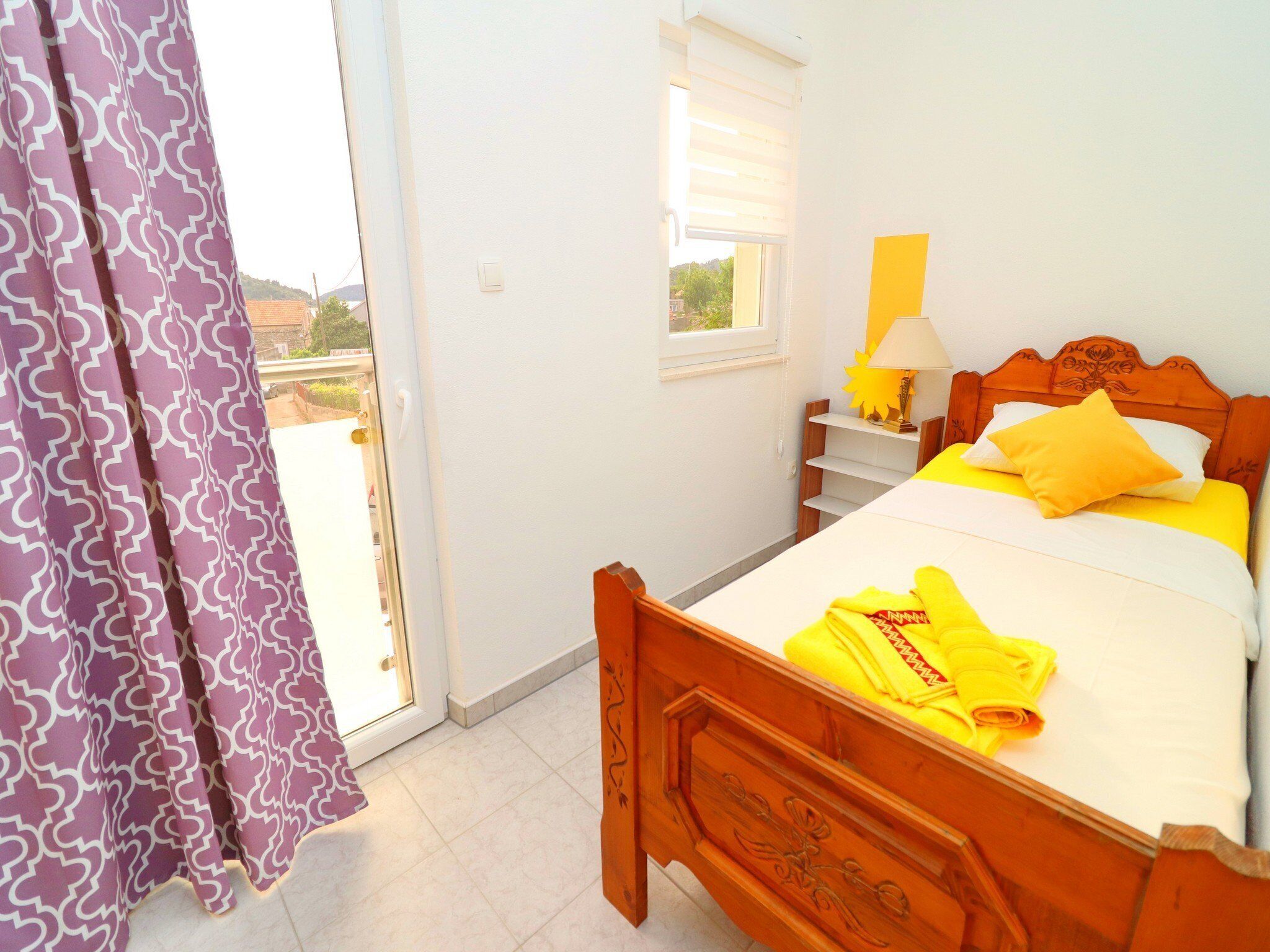 A bedroom with a wooden bed, a nightstand with a lamp, and a window with blinds.