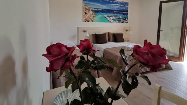A bedroom with a bed, a painting of a coastal scene, and a vase with red roses. - Paluna (Otranto)