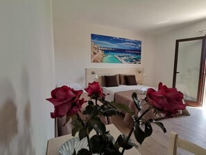 A bedroom with a bed, a painting of a coastal scene, and a vase with red roses. - Paluna (Otranto)