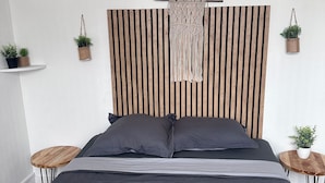 A modern bedroom with a large bed, a wooden headboard, and two small side tables with potted plants.