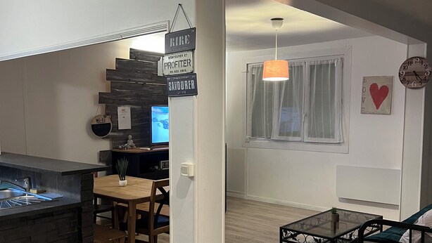 A modern kitchen with a built-in island, a dining area with a wooden table and chairs, a small black coffee table, and a cozy seating area with a sofa and a patterned rug.