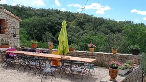 An outdoor patio with a stone wall, a wooden table, metal chairs, and potted plants. - Les Gîtes du mas Champion (Saint-Just-et-Vacquières)