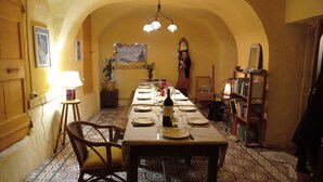 A dining area with a long table set for four, a chandelier, and a bookshelf with books. - Les Gîtes du mas Champion (Saint-Just-et-Vacquières)