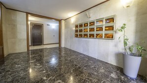 Un hall d’entrée avec un sol en marbre, un comptoir de réception, un luminaire fixé au mur et une plante en pot.