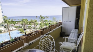 Un balcon donnant sur une piscine et des palmiers, avec des chaises en métal blanc et une petite table.