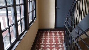 Un pasillo estrecho con piso estampado, una puerta y una escalera con barandillas de metal.