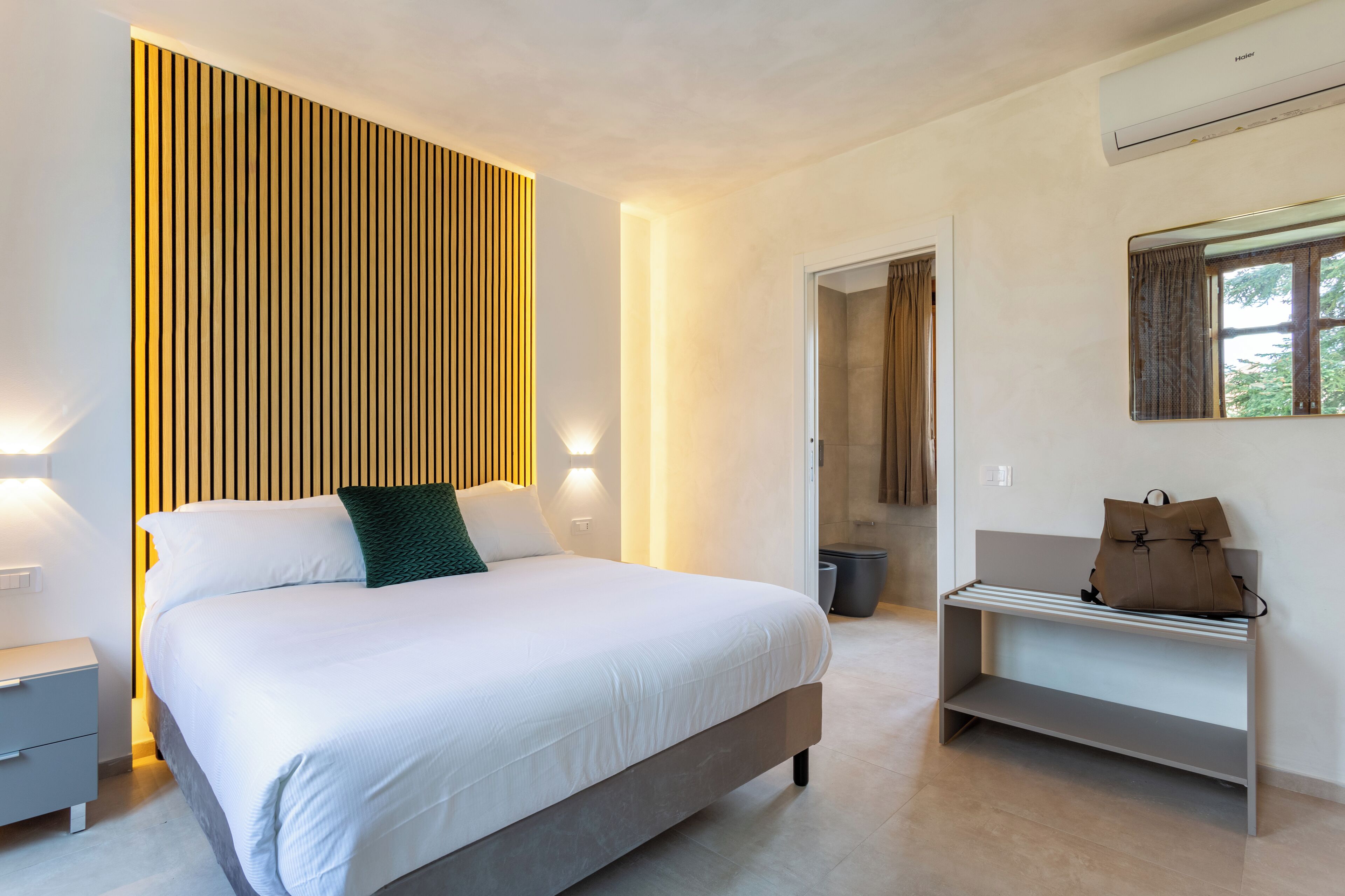 Una camera da letto moderna con un letto grande, lampade sui comodini, una panca con una borsa e una finestra con tende.