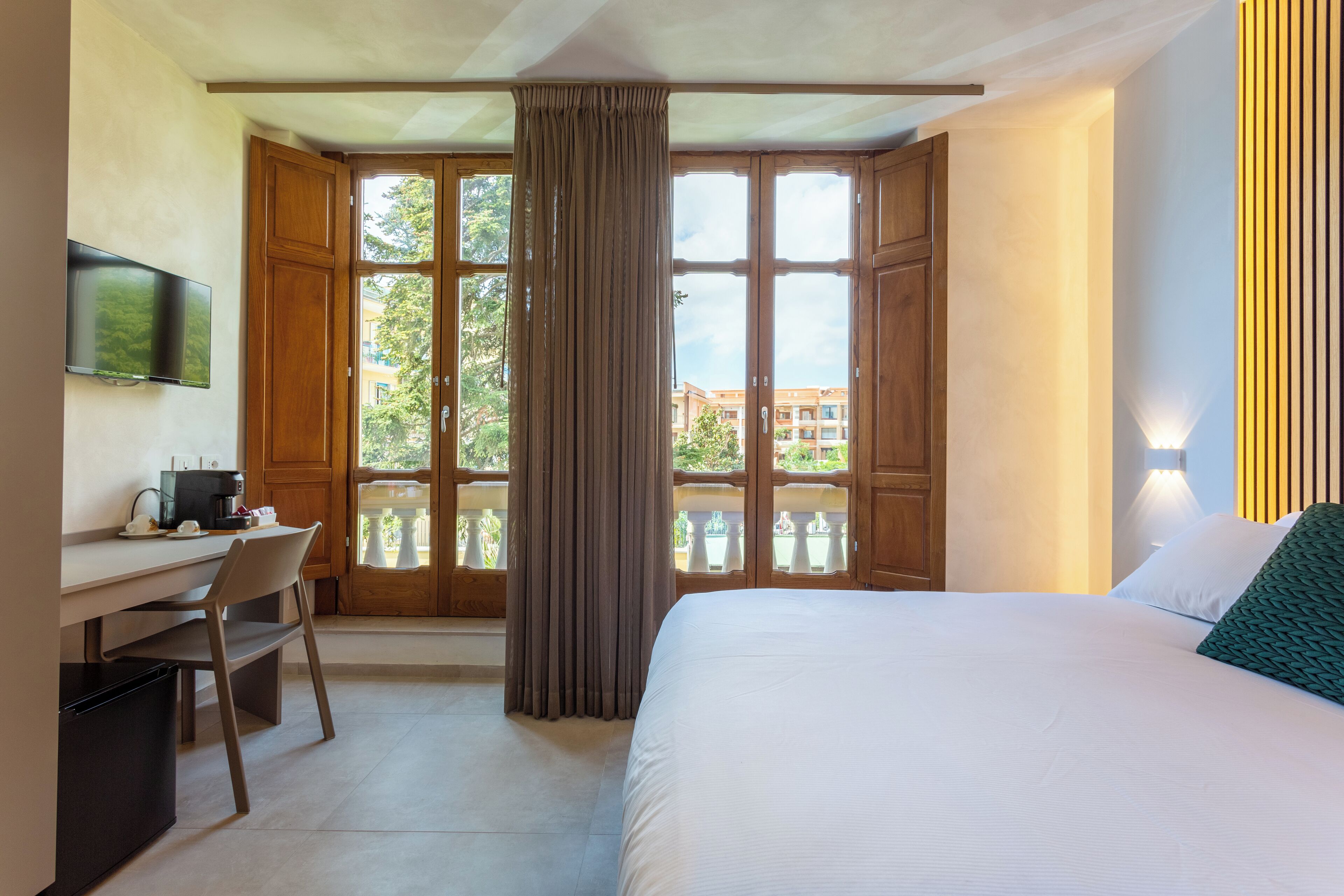 A hotel room with a bed, a desk with a chair, a television, and a window with curtains.