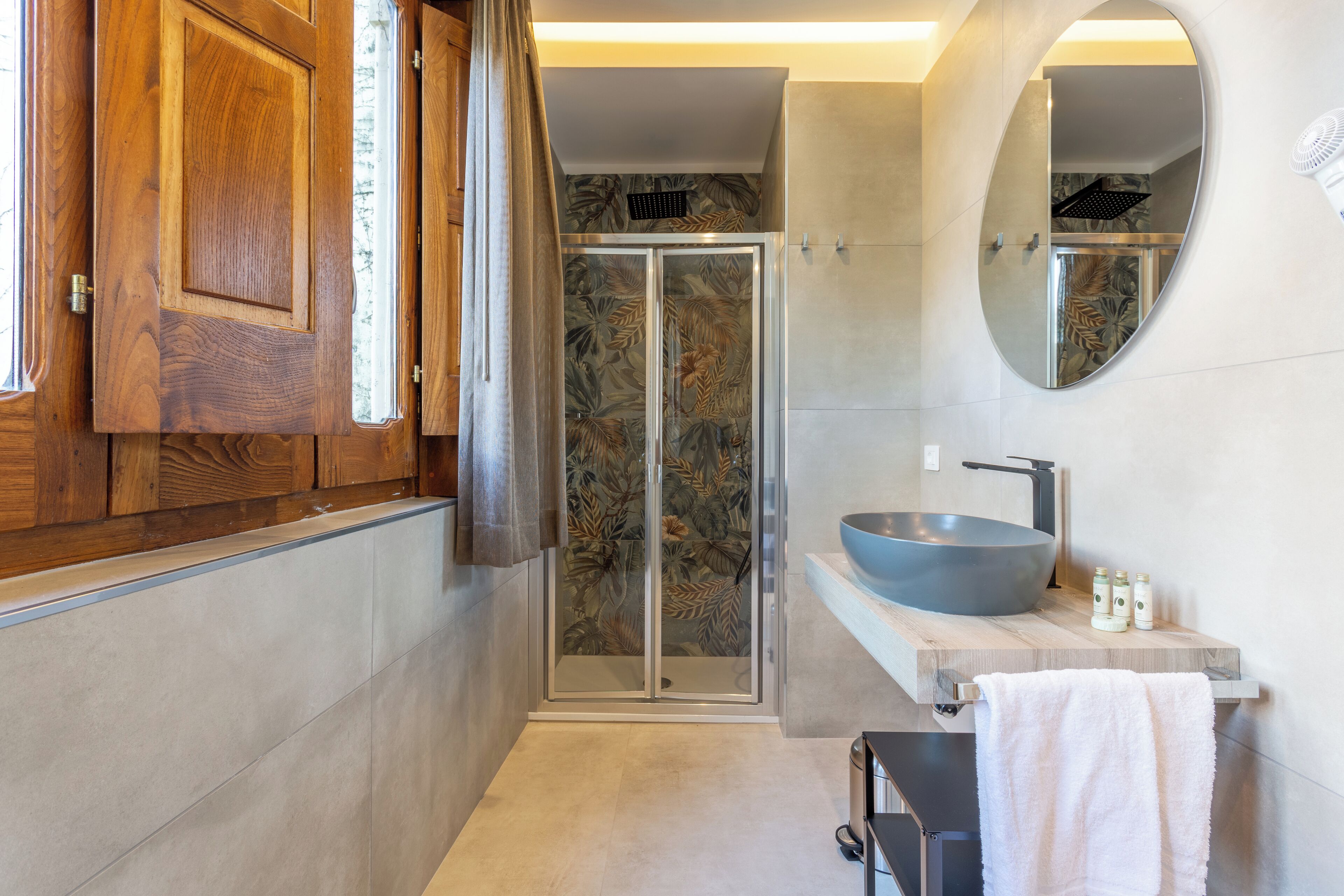 A modern bathroom with a wooden vanity, a large mirror, a glass shower enclosure, and a large sink.