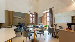 A modern dining area with a long counter, multiple tables, and chairs. There are potted plants on the tables and a large mirror on the wall. - Villa Cipriano - Relais di Charm (Naples)