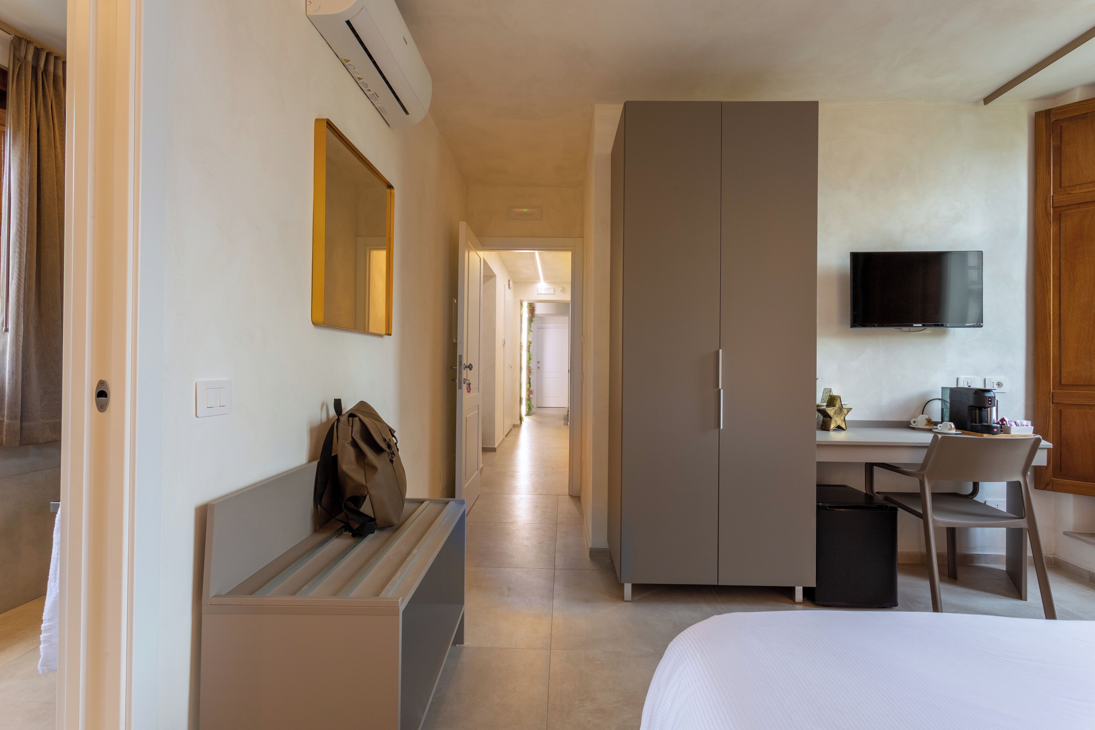 Habitació d'hotel amb un llit, un escriptori amb cadira, un armari, un televisor i un mirall.