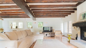 A living room with a beige sectional sofa, a flat-screen TV, a fireplace, and a stone fireplace surround. - Beautiful Normand-style house with pool, 3 minutes from the beach (Auberville)