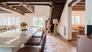 A spacious dining area with a long table and benches, wooden beams on the ceiling, and large windows with natural light. - Beautiful Normand-style house with pool, 3 minutes from the beach (Auberville)