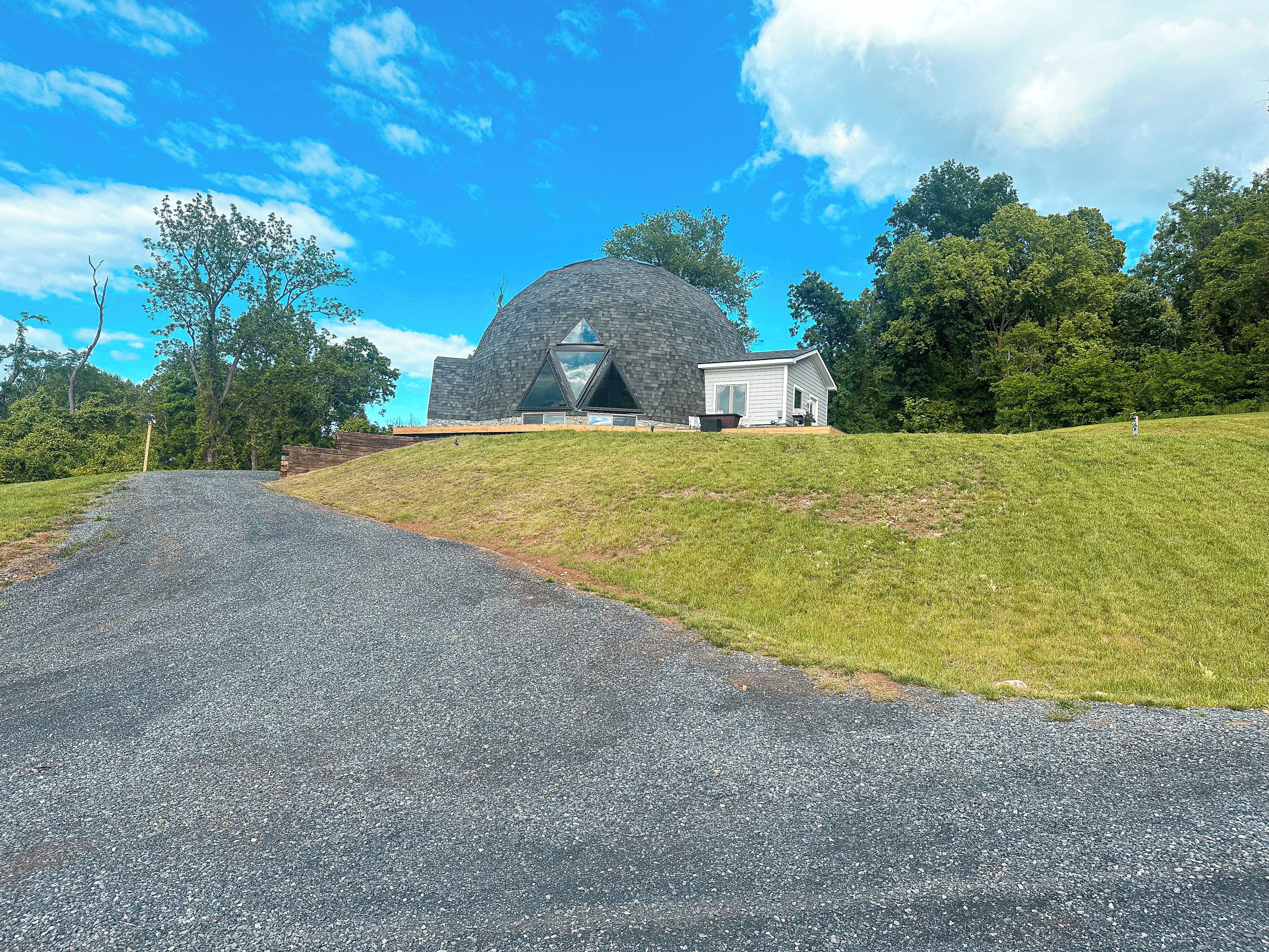 A modern building with a unique geodesic dome structure, a small adjacent house, and a gravel driveway leading to the entrance.