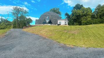 A modern building with a unique geodesic dome structure, a small adjacent house, and a gravel driveway leading to the entrance.
