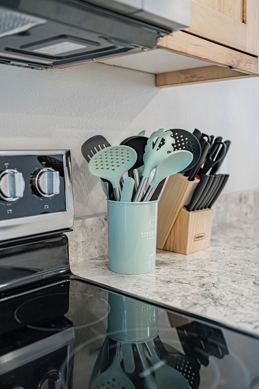 A kitchen counter with a stainless steel stove, a light blue utensil holder, and a wooden knife block.