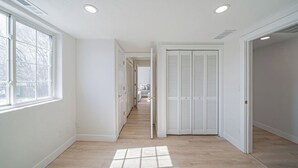 Een gang met witte wanden, houten vloeren en een deur naar een kamer met witte luiken.