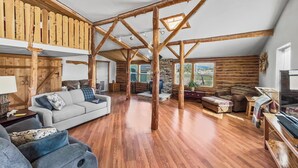 Un'ampia zona giorno con travi in legno, una camera soppalcata e un'ampia finestra che offre vista sull'esterno.