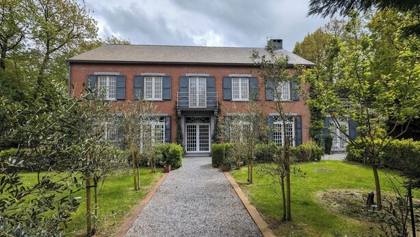 Une maison à deux étages, construite en briques, avec une allée en gravier et un petit jardin.
