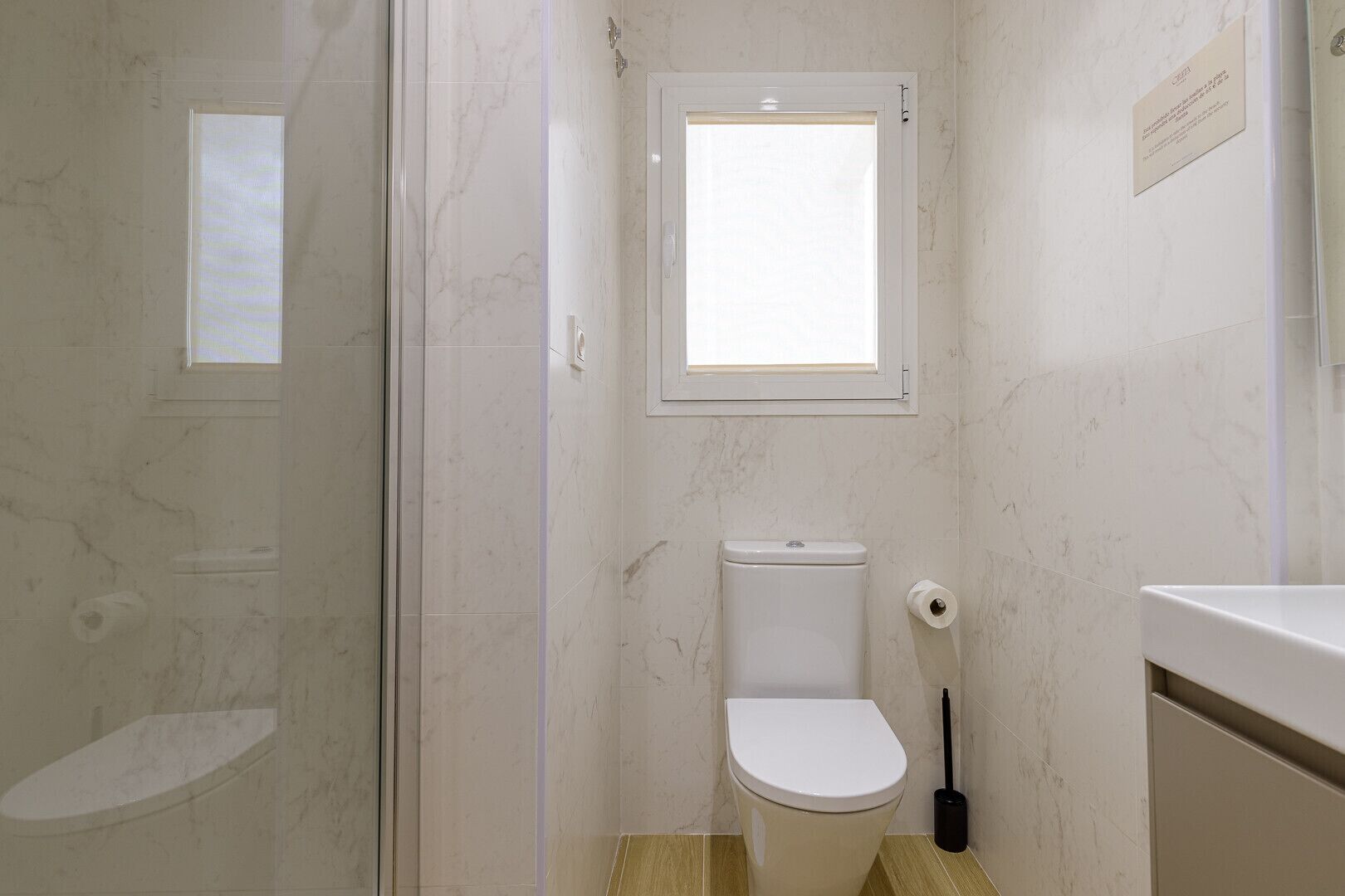 A bathroom with a toilet, a window, and a shower area.