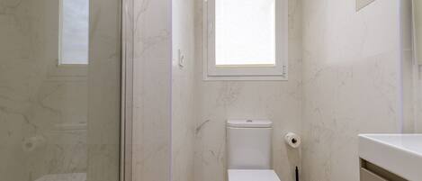 A bathroom with a toilet, a window, and a shower area.