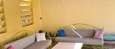 A room with two green metal sofas, a white table, and a ceiling fan.