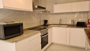 Een moderne keuken met witte kastjes, een roestvrijstalen magnetron, een koffiezetapparaat, een broodrooster en een spoelbak.