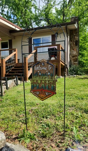 Une enseigne accueillante pour « Pupper’s Place », avec un escalier en bois et une maison en pierre en arrière-plan.