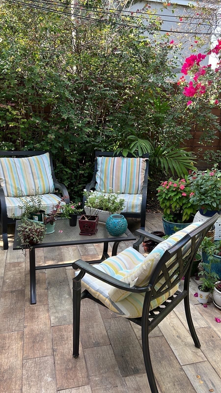 A patio with two striped chairs, a glass table, and various potted plants.