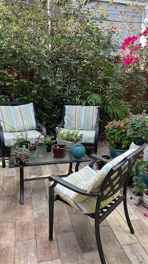 Une terrasse avec deux chaises à rayures, une table en verre et diverses plantes en pot.