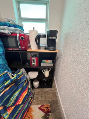 Une petite pièce, de taille modeste, comprenant un lit, un four à micro-ondes, une machine à café, un grille-pain et une étagère contenant divers objets.
