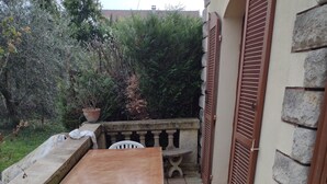 An outdoor patio with a wooden table and white chairs, a stone wall, and a tiled floor. - Belle Chambre Chaleureuse au Calme (Chennevières-sur-Marne)